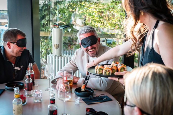 Gast mit Augenbinde bekommt bei einer Blindverkostung Sushi gereicht