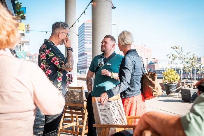 Gäste mit Drinks im Außenbereich vor der Überseestadt-Kulisse