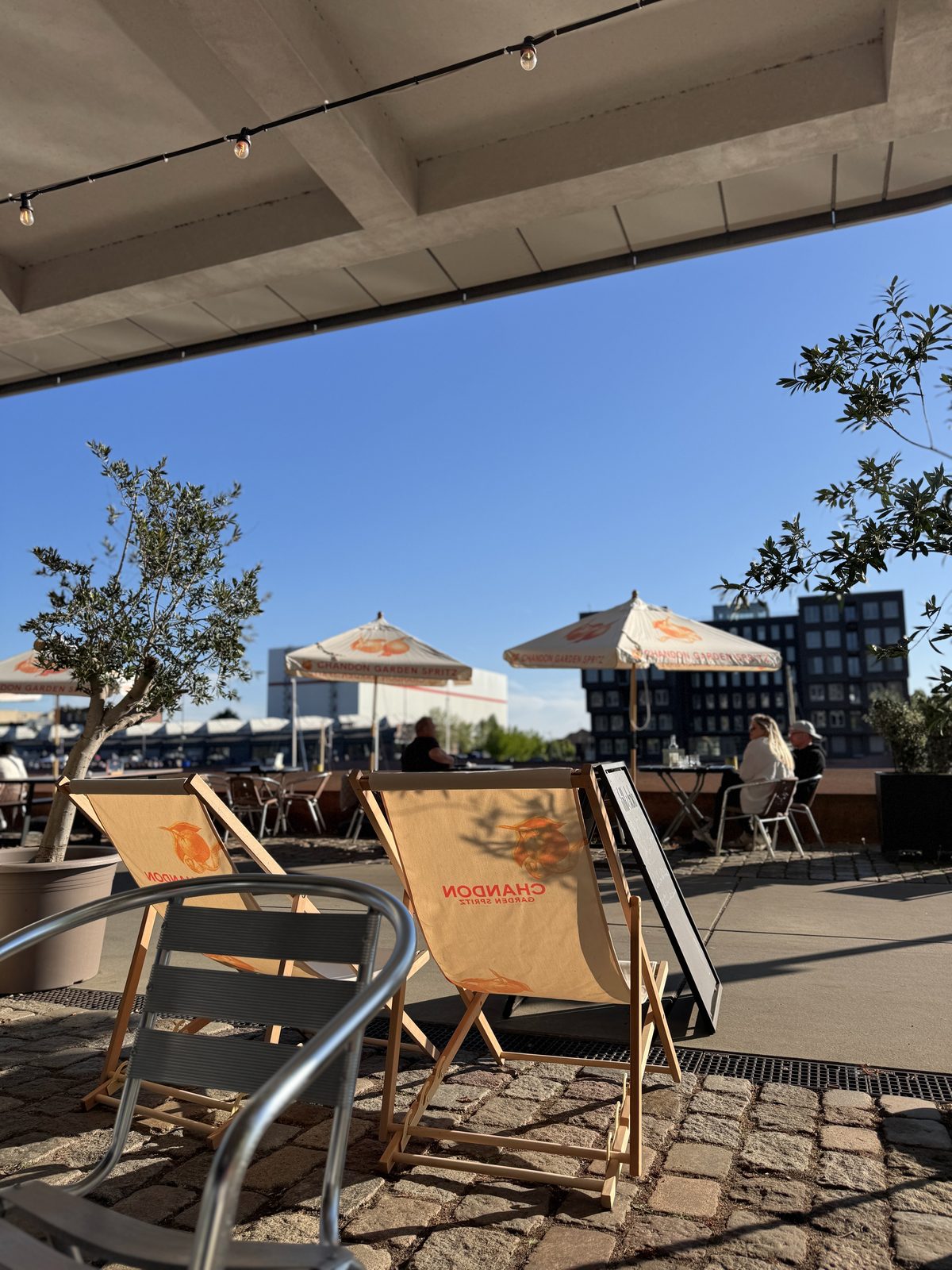 Außenbereich des BOME Studio Bremen mit Sonnenschirmen, Liegestühlen und Blick auf die Überseestadt
