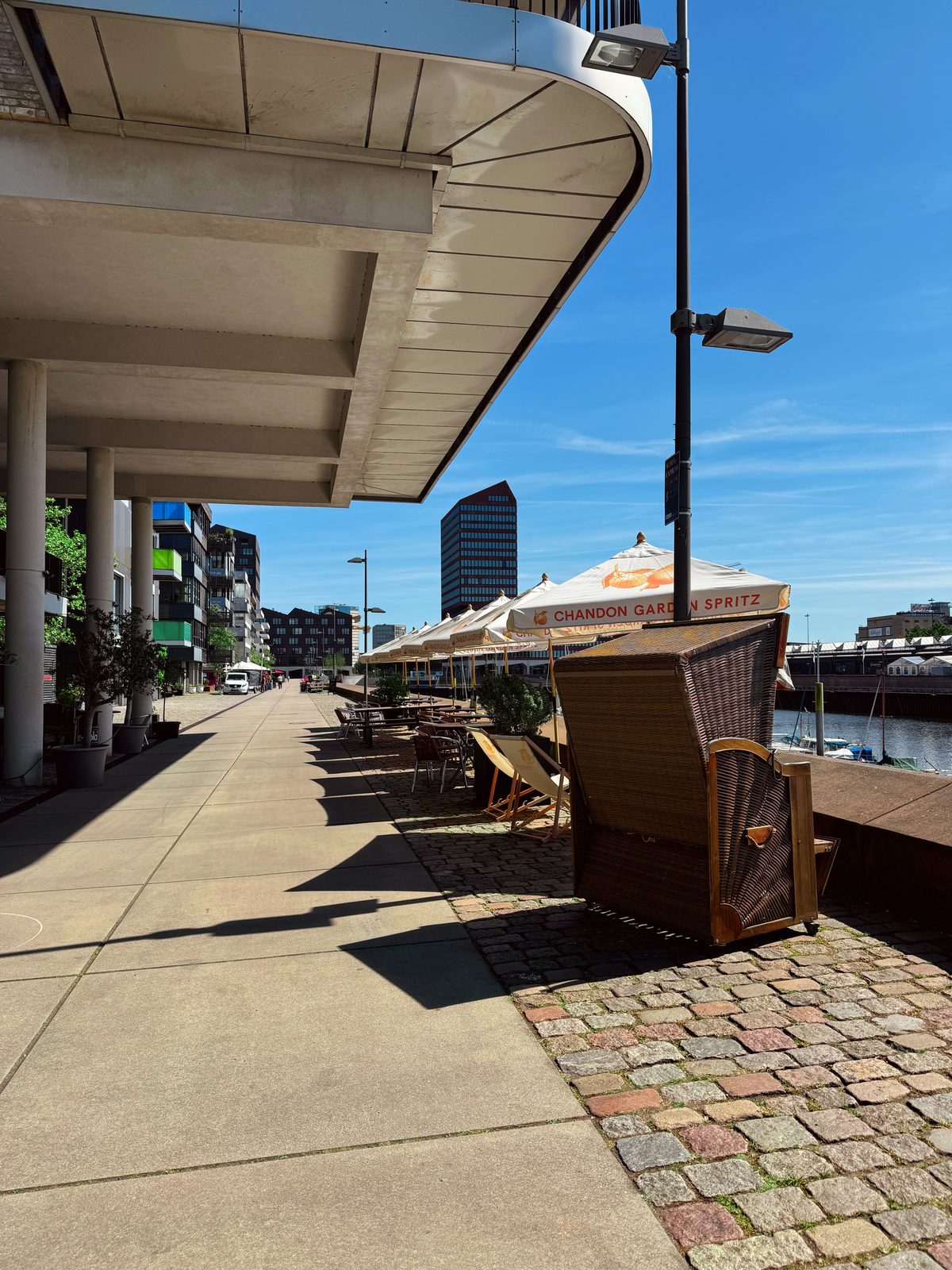 Promenade vor dem BOME Studio Bremen mit überdachter Arkade, Sonnenschirmen und Blick auf das Hafenbecken